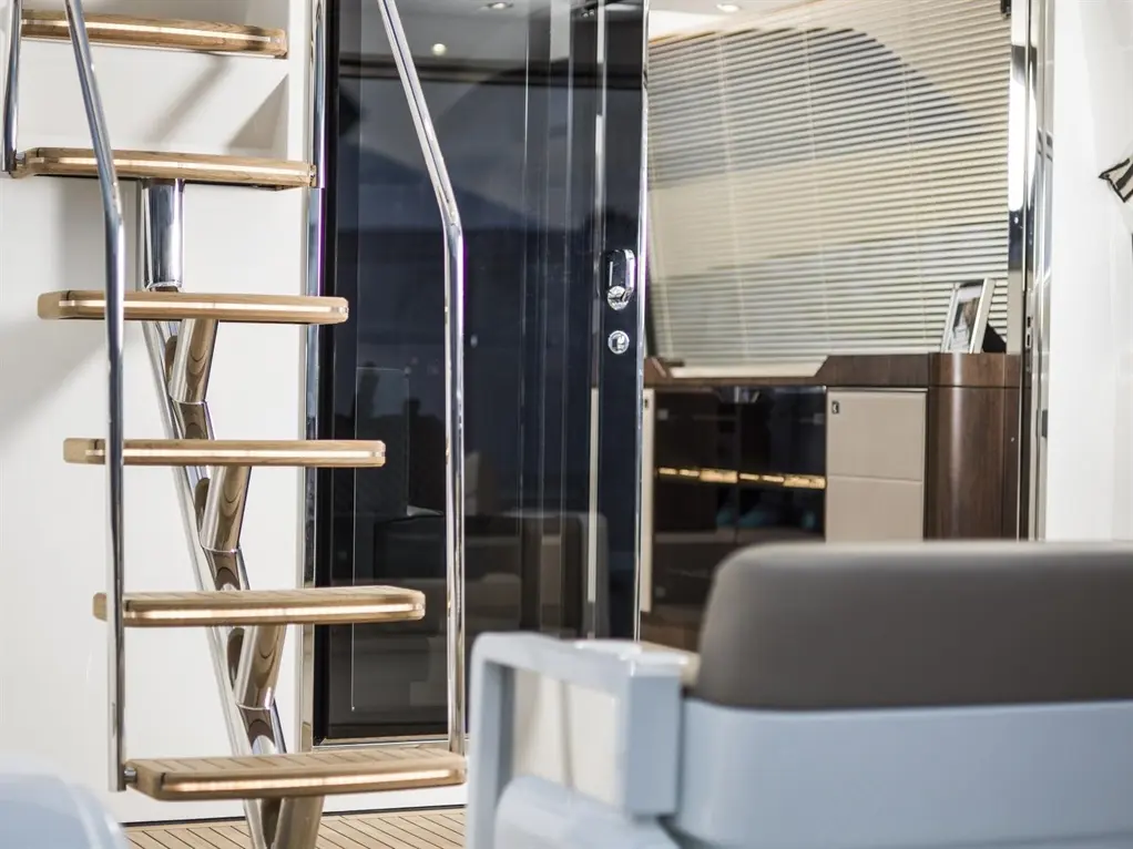 Modern yacht interior featuring a sleek, chrome and wood spiral staircase leading to a glass door and stylish furniture.